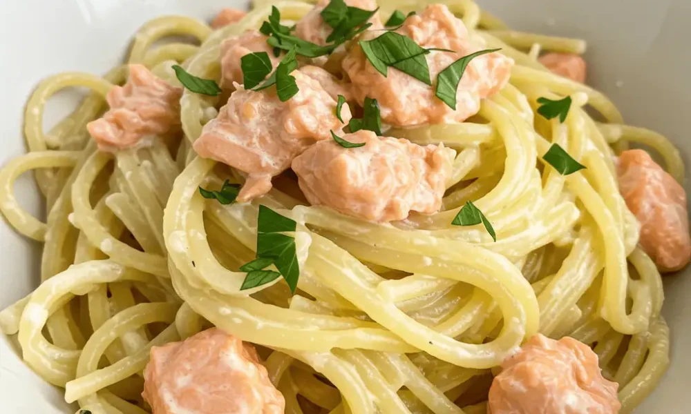 creamy garlic butter salmon pasta in a white bowl with flaked salmon and herbs